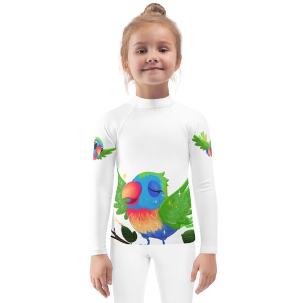 A smiling child wearing a white long-sleeve rash guard featuring a vibrant, colorful parrot design with green wings and a peaceful expression, printed on the front and sleeves.